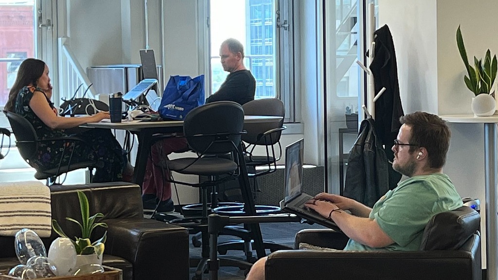Woman and man sitting at a tall table with a man sitting in a chair working on a laptop.