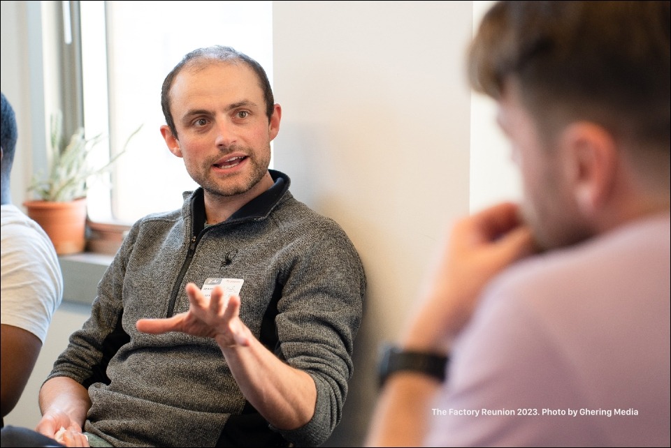 A Factory member wearing a grey fleece zipper sweater has a conversation with another Factory member.