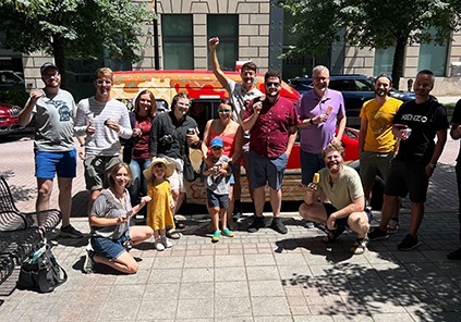 Several community members standing in front of a ice cream truck during a sunny summer day.