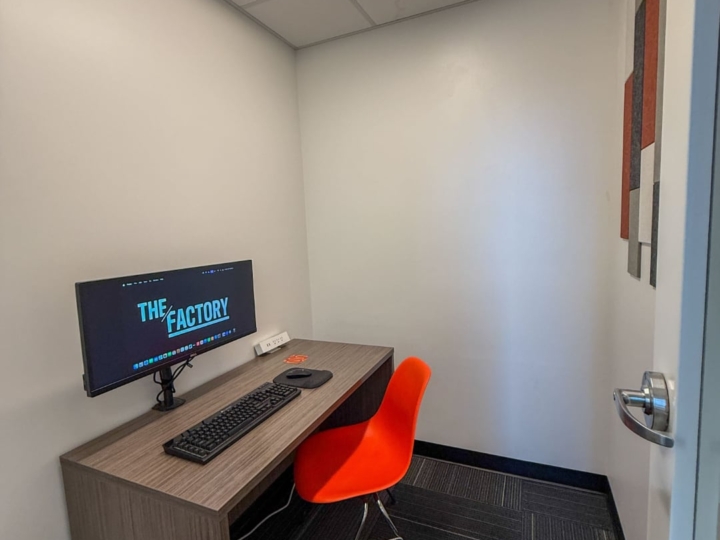 Photo of The Factory video call booth with an orange plastic chair and an a wooden desk placed on the west side of the room