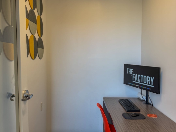 Photo of The Factory video call booth with an orange plastic chair and an a wooden desk placed on the east side of the room